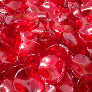 May include: A large pile of red, translucent plastic heart-shaped sequins. The sequins are shiny and have a slight curve to them.