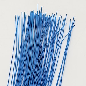 Puede incluir: Un manojo de alambre floral azul, fino y recto. Los alambres están muy juntos, creando un grupo denso. Los alambres son de un color azul sólido y vibrante, y están colocados sobre un fondo blanco liso.