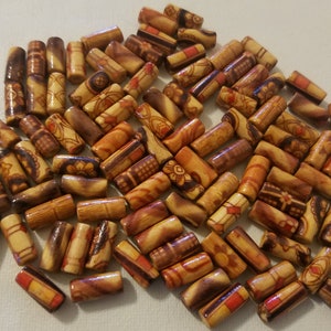 May include: A collection of wooden beads with intricate patterns in shades of brown, orange, and red. The beads are cylindrical and have a smooth, polished finish.