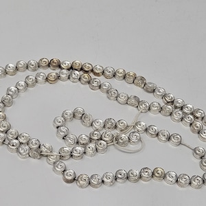 Pode incluir: Um colar de contas de prata e ouro com um design em espiral em cada conta. O colar é feito de metal e mede aproximadamente 152 cm de comprimento.