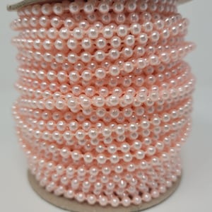 May include: A spool of pale pink pearl trim. The trim is made of small, round pearls that are strung together on a thin thread. The pearls are a light, almost white, pink color.