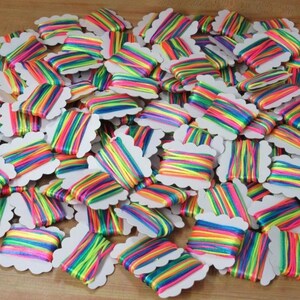 May include: A collection of rainbow-coloured embroidery floss spools. Each spool displays a vibrant spectrum of colours, including red, orange, yellow, green, blue, and purple. The floss is neatly wound on white, scalloped-edge cards, creating a colourful display.