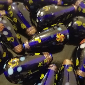 May include: A collection of blue glass beads with white and yellow floral patterns. The beads are teardrop shaped and have a glossy finish.