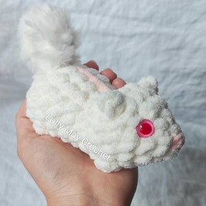 Puede incluir: Un animal de peluche tejido a ganchillo en color blanco con una cola esponjosa, ojos de pl&aacute;stico rosa y una peque&ntilde;a nariz rosa. El texto Lolly May Crochet est&aacute; impreso en el costado del cuerpo de hilo blanco. Hecho de hilo blanco grueso y suave.