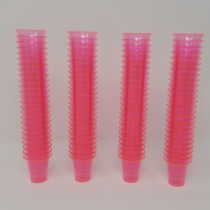 May include: A stack of 40 bright pink plastic shot glasses. The glasses are stacked in four columns of ten glasses each.