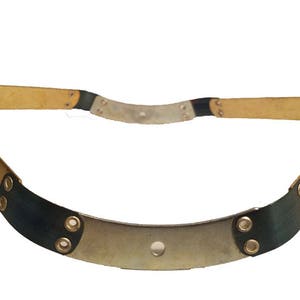 May include: A gold-colored metal band with black leather accents and a single hole in the center. The band is curved and has a slightly rounded shape.