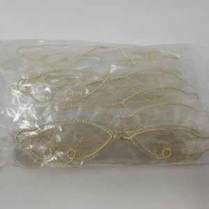 Op de afbeelding: Een doorzichtige plastic verpakking met meerdere goudkleurige, draadomrande engelen vleugels. De vleugels hebben een delicaat, filigraan ontwerp. Ze zijn waarschijnlijk bedoeld voor knutselprojecten of kostuumaccessoires.