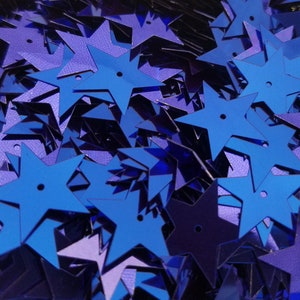 May include: A pile of blue star-shaped sequins. The sequins are shiny and have a metallic finish.