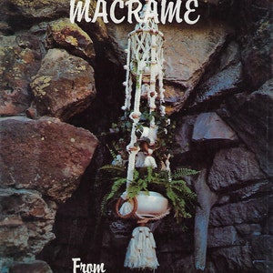 Puede incluir: Un macetero de macramé blanco con una maceta blanca y una planta verde colgando de una pared de piedra. El texto "A Sip Of Macrame From Brandy's" está impreso en la imagen.