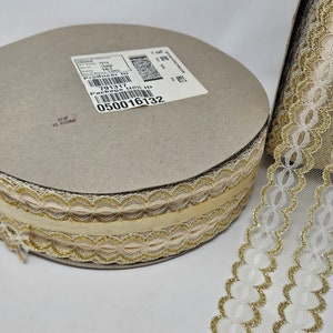 Op de afbeelding: Een spoel met witte en gouden kant met een gouden glitterafwerking. De kant heeft een gegolfde rand en een delicaat bloemenpatroon. De spoel is gelabeld met een product-ID en een verpakkingseenheid-ID.