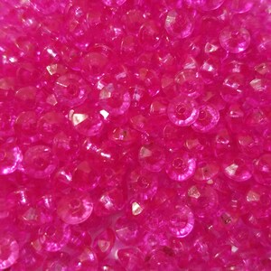 May include: A collection of small, round, translucent hot pink beads with a faceted surface texture. Each bead features a central hole for threading, creating a uniform appearance of bright, reflective pink circular shapes packed together.