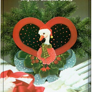 Puede incluir: Una decoraci&oacute;n navide&ntilde;a de madera en forma de coraz&oacute;n pintada a mano con un ganso que lleva un gorro de Pap&aacute; Noel y una bufanda a cuadros. El ganso est&aacute; rodeado de bayas rojas y hojas verdes. El coraz&oacute;n est&aacute; decorado con lunares negros y blancos y un borde rojo.