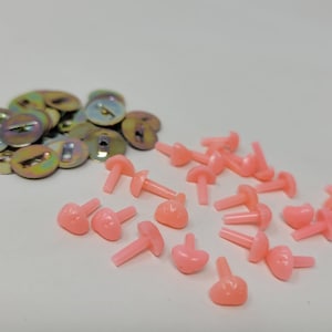 May include: A collection of craft supplies, including small, iridescent metal washers and pink plastic doll eyes in a variety of shapes. The eyes have a heart shape and a rounded shape.