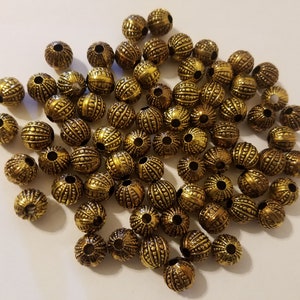 May include: A large group of gold-colored metal beads with a textured surface. The beads are round and have a hole in the center for stringing.
