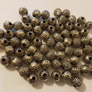 May include: A large pile of silver metal beads with a textured surface. The beads are round and have a hole in the center.