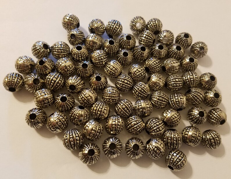 May include: A large pile of silver metal beads with a textured surface. The beads are round and have a hole in the center.