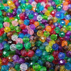 May include: A large assortment of colorful faceted glass beads. The beads are various shades of red, orange, yellow, green, blue, purple, and clear. The beads are all approximately the same size and shape.