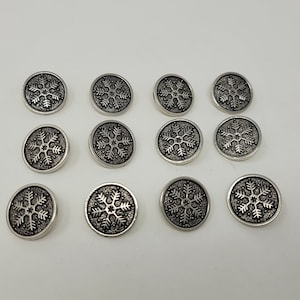Op de afbeelding: Twaalf zilveren sneeuwvlokkenknopen met een zwart sneeuwvlokkenontwerp.