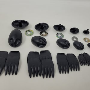May include: An assortment of black plastic components, including oval-shaped pieces with posts, rounded shapes, star washers, and foot-shaped parts with multiple prongs. The items are arranged on a white surface.