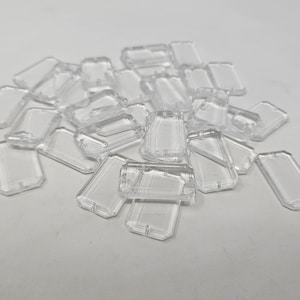 Op de afbeelding: Een stapel doorzichtige rechthoekige plastic vormen, mogelijk voor knutselen of het maken van sieraden.