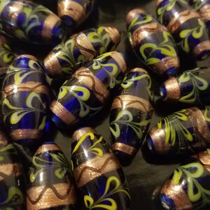 May include: A collection of blue and gold glass beads with a swirling pattern. The beads are oval shaped and have a glossy finish.