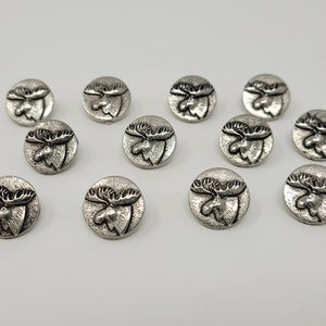 Puede incluir: Doce botones plateados con un diseño de cabeza de alce. Los botones son redondos y tienen un diseño de cabeza de alce en relieve.