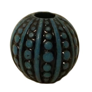 May include: A teal blue and black round bead with a textured surface. The bead has a hole in the center for stringing.