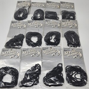 May include: Multiple packages of black simulated pearl bead strands. Each package is labeled "String Alongs" with the words "Simulated Pearl" printed below. The beads are strung together and packaged in clear plastic.