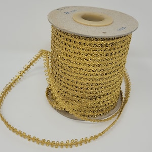 May include: A spool of gold metallic trim with a scalloped edge. The trim is wound around a cardboard spool with the text "1/2" and "X 100" printed on it.