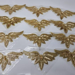 Puede incluir: Doce apliques de mariposa de color dorado, con cuentas y lentejuelas. Cada aplique tiene una cuenta central redonda y elevada.