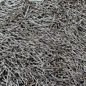 May include: A close-up of a pile of shiny, silver cotter pins. The pins are made of metal and have a looped end and two prongs. The pins are scattered and overlapping, creating a dense, textured surface.