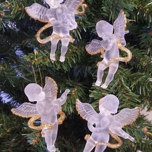 May include: Four frosted glass angel ornaments with gold glitter wings and a gold glitter halo. The angels are holding musical instruments.