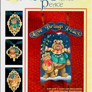 May include: A decorative sign with the text "Love Brings Peace" and a painting of two bears in winter attire. The image also includes three laser-cut ornaments with bear designs, perfect for holiday decorating.
