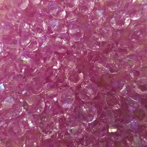 May include: A collection of small, translucent, light purple beads with a faceted, diamond-like cut. Each bead features a central hole and a reflective surface that catches the light, creating a sparkling, multi-dimensional appearance.