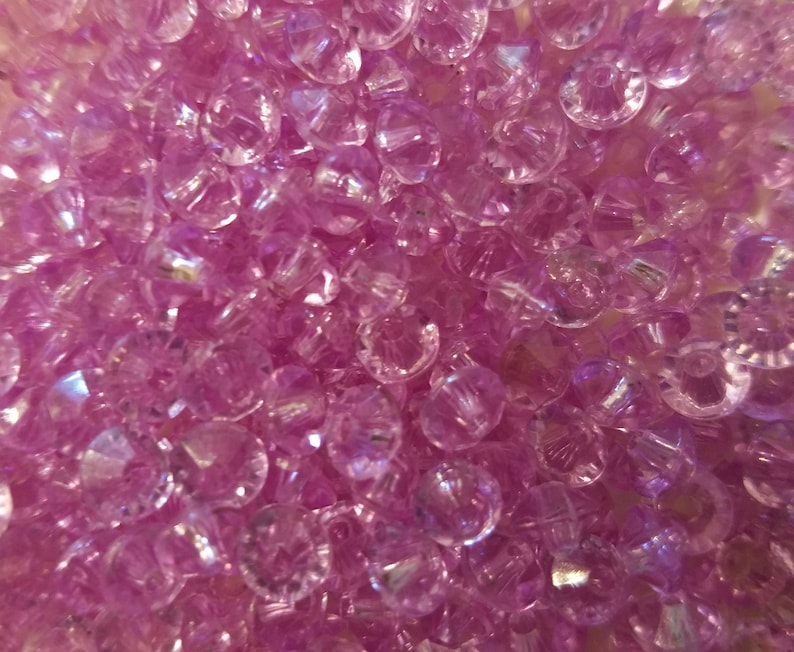 May include: A collection of small, translucent, light purple beads with a faceted, diamond-like cut. Each bead features a central hole and a reflective surface that catches the light, creating a sparkling, multi-dimensional appearance.