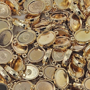 May include: A pile of gold-colored oval bezel settings for jewelry making. Each setting has a loop on each side for attaching to other components. The settings are empty and ready to be filled with resin or other materials.