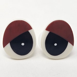 Puede incluir: Dos ojos saltones de plástico con detalles blancos, negros y marrones. Los ojos son redondos y tienen una pupila blanca con un centro negro.