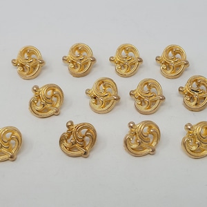 May include: A set of 12 gold-toned metal decorative embellishments with a swirling, ornate design. The embellishments are perfect for adding a touch of elegance to crafts, jewelry, and other projects.