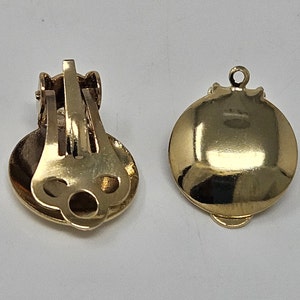 Peut inclure: Deux boucles d'oreilles dorées à clip. Chaque boucle d'oreille a une face ronde et polie et un mécanisme à clip à l'arrière. Les boucles d'oreilles sont probablement en métal et ont une finition brillante. Le design est simple et élégant.