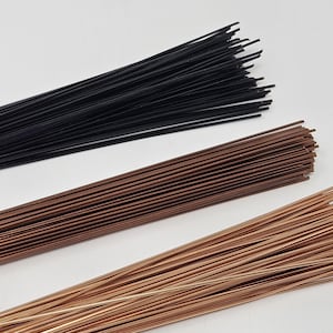 Könnte beinhalten: Drei Bündel Blumendraht in Schwarz, Braun und Kupfer. Die Drähte sind dünn und gerade, in parallelen Linien angeordnet und werden wahrscheinlich für Bastelarbeiten oder Blumengestecke verwendet.