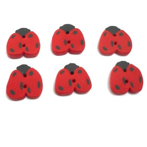 Peut inclure: Six boutons rouges en forme de coccinelle, avec des points noirs et des têtes grises, sont disposés sur un fond blanc. Chaque bouton a deux trous pour la couture. Ces boutons décoratifs sont parfaits pour les projets d'artisanat.