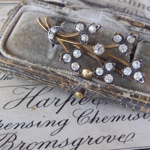 May include: A vintage gold and silver brooch with a delicate floral design featuring a cluster of clear rhinestones. The brooch is displayed in a velvet-lined box.