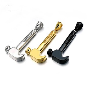 Puede incluir: Tres collares con colgante de martillo en plata, oro y negro. Cada collar presenta un diseño de martillo detallado con una superficie texturizada.