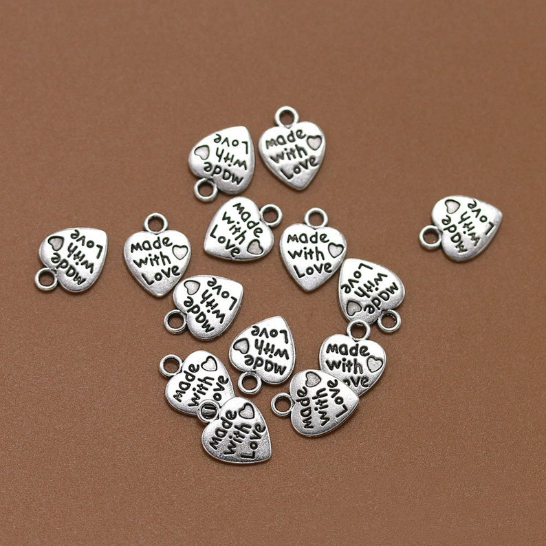 May include: Silver heart-shaped charms with the text "Made with Love" and "Love with a little arrow" printed on them.