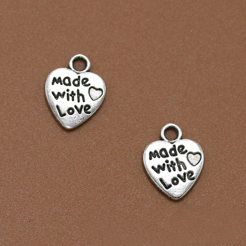 May include: Two silver heart-shaped charms with the words "Made with Love" and a small heart design.