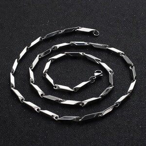 K&ouml;nnte beinhalten: Eine silberne Kettenkette mit geometrischem Gliederdesign. Die Kette ist aus Edelstahl und hat eine polierte Oberfl&auml;che.