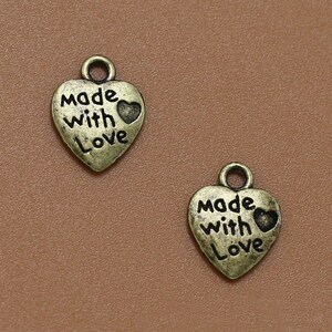 May include: Two antique gold heart-shaped charms with the words "made with love" and a small heart design.