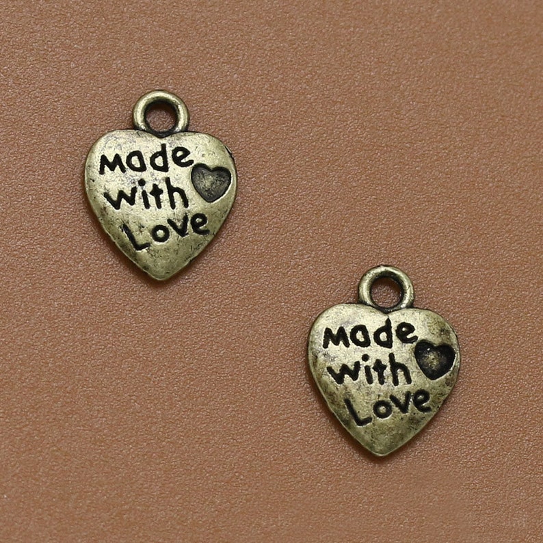 May include: Two antique gold heart-shaped charms with the words "made with love" and a small heart design.