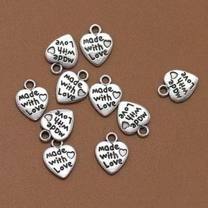 May include: A collection of silver-toned heart-shaped charms with the text "Made with Love" on each charm.