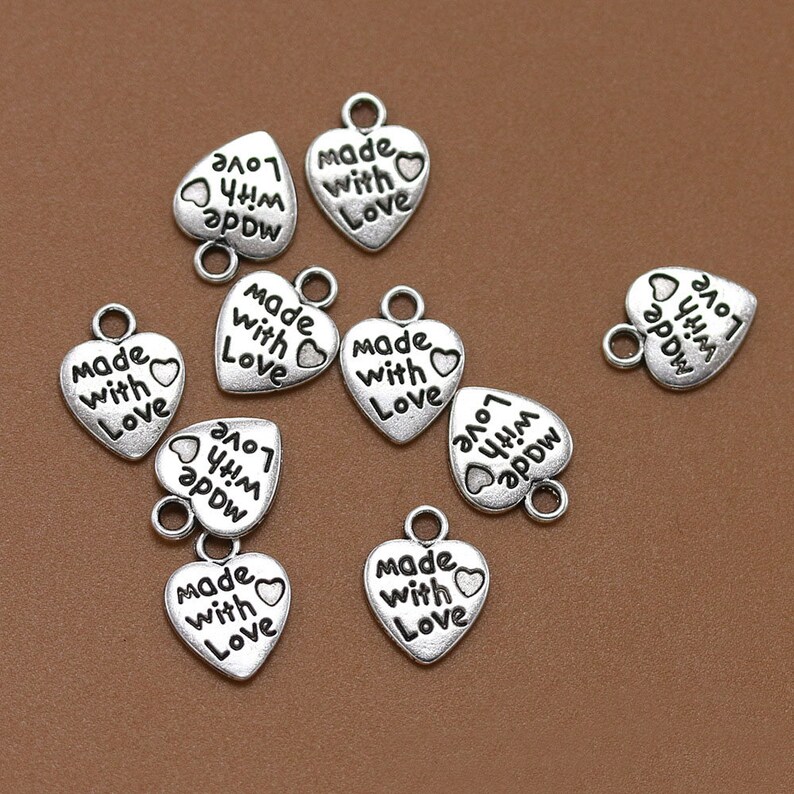 May include: A collection of silver-toned heart-shaped charms with the text "Made with Love" on each charm.